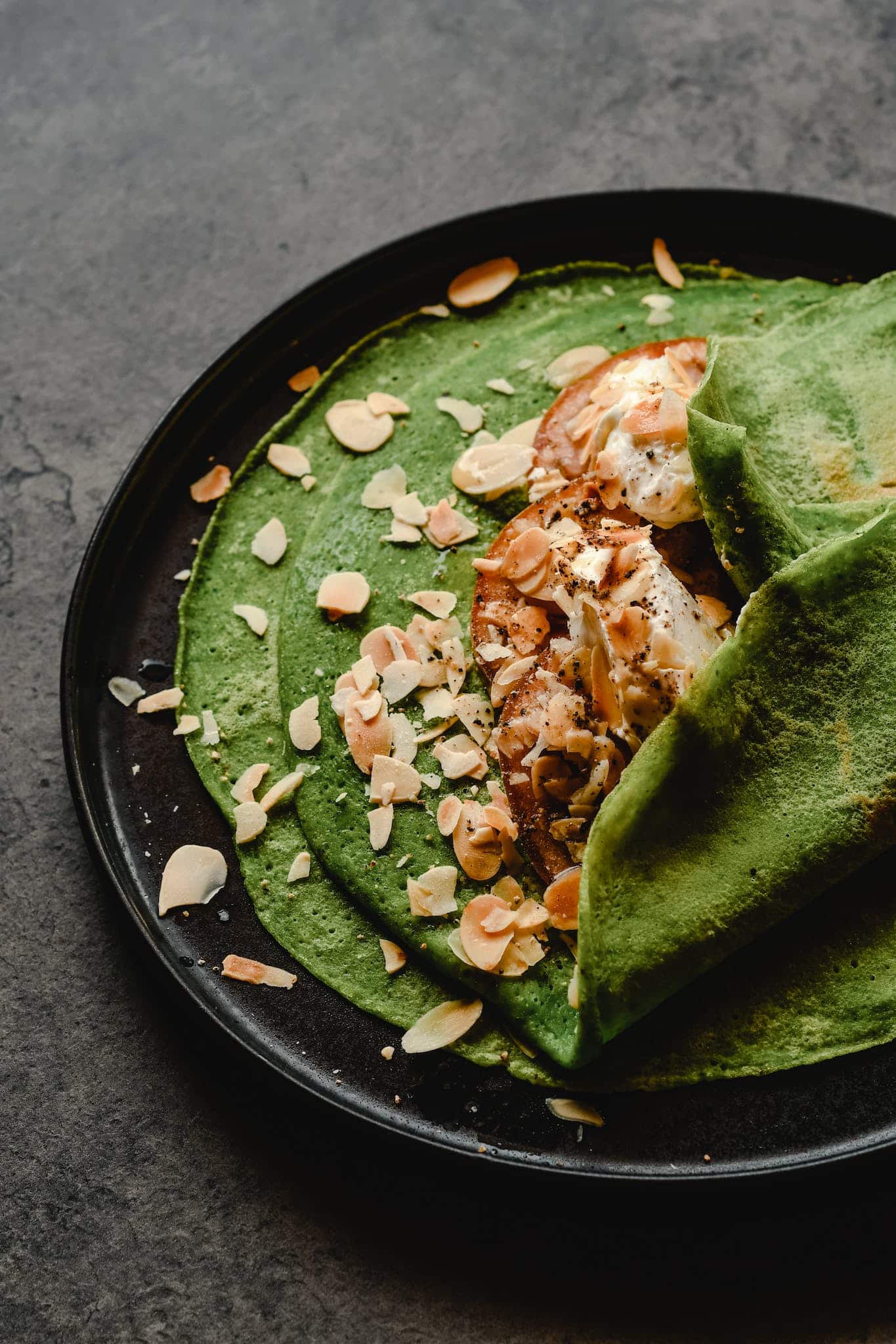 Green Crepes with Almond Flakes on Black Ceramic Plate